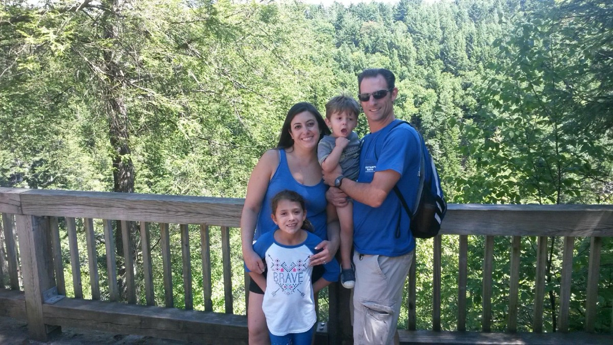 A mom, a dad, a girl in a BRAVE shirt and a toddler on the dad's hip at the overlook railing.