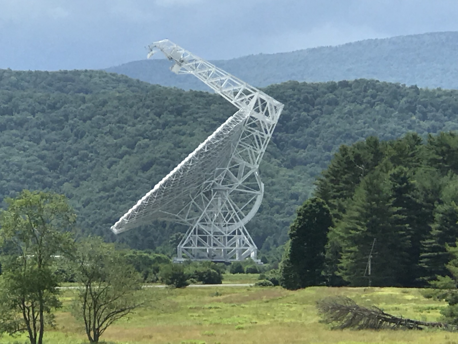 The Robert C. Byrd Green Bank Telescope, an enormous white steel dish on an angled lattice frame, standing in a green valley with forested ridges rising behind it.