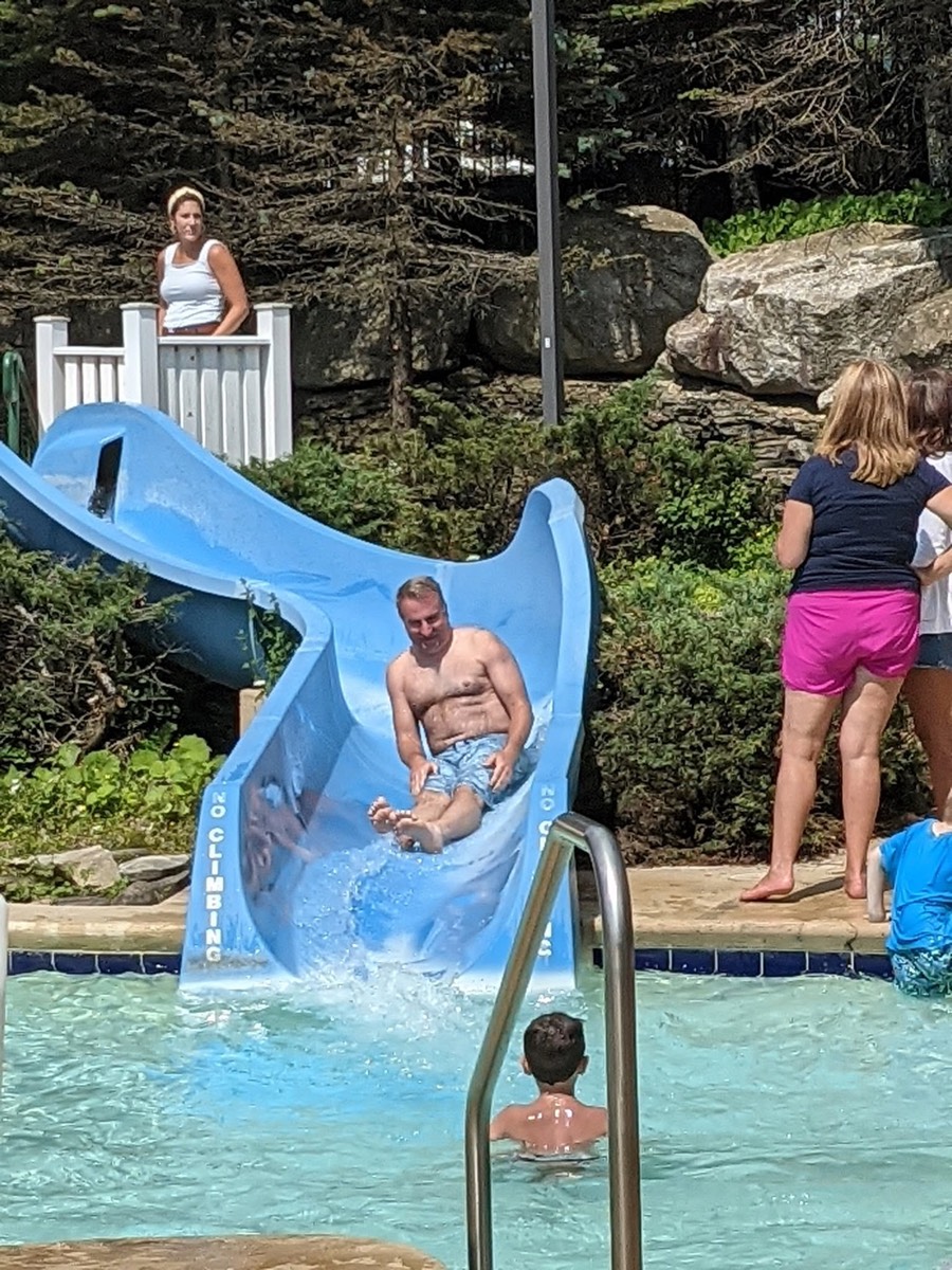 A man coming down the blue waterslide on his back, a woman watching from the deck above.