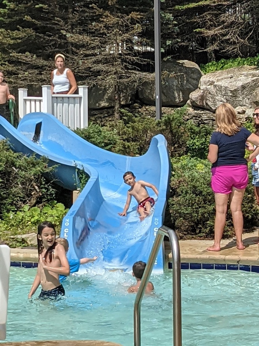 A boy emerging from the waterslide into the pool with a girl already in the water in front of him.