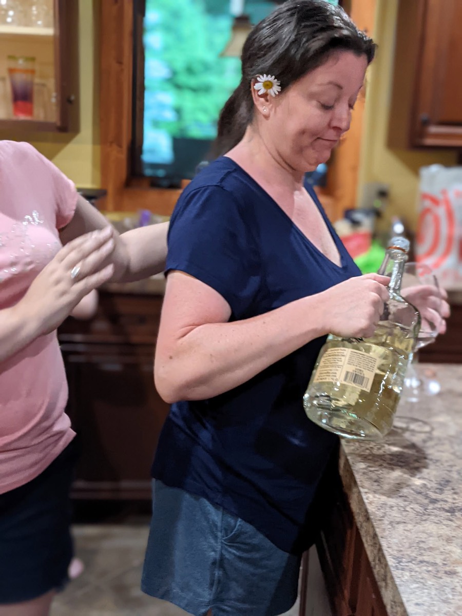 A woman with a daisy tucked behind her ear pouring from a bottle at the kitchen counter.