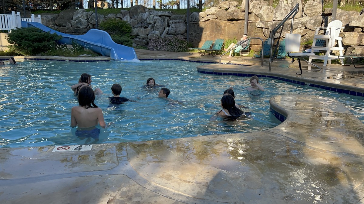 Children swimming in a resort pool with a blue water slide and landscaped rock features around the edge.