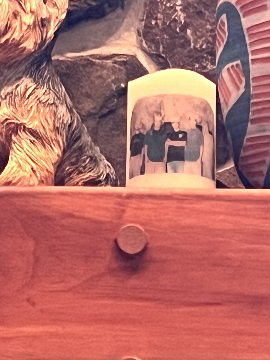 A white mug printed with a photograph of a group of people standing arm in arm, sitting on a wooden ledge in front of a stone wall.