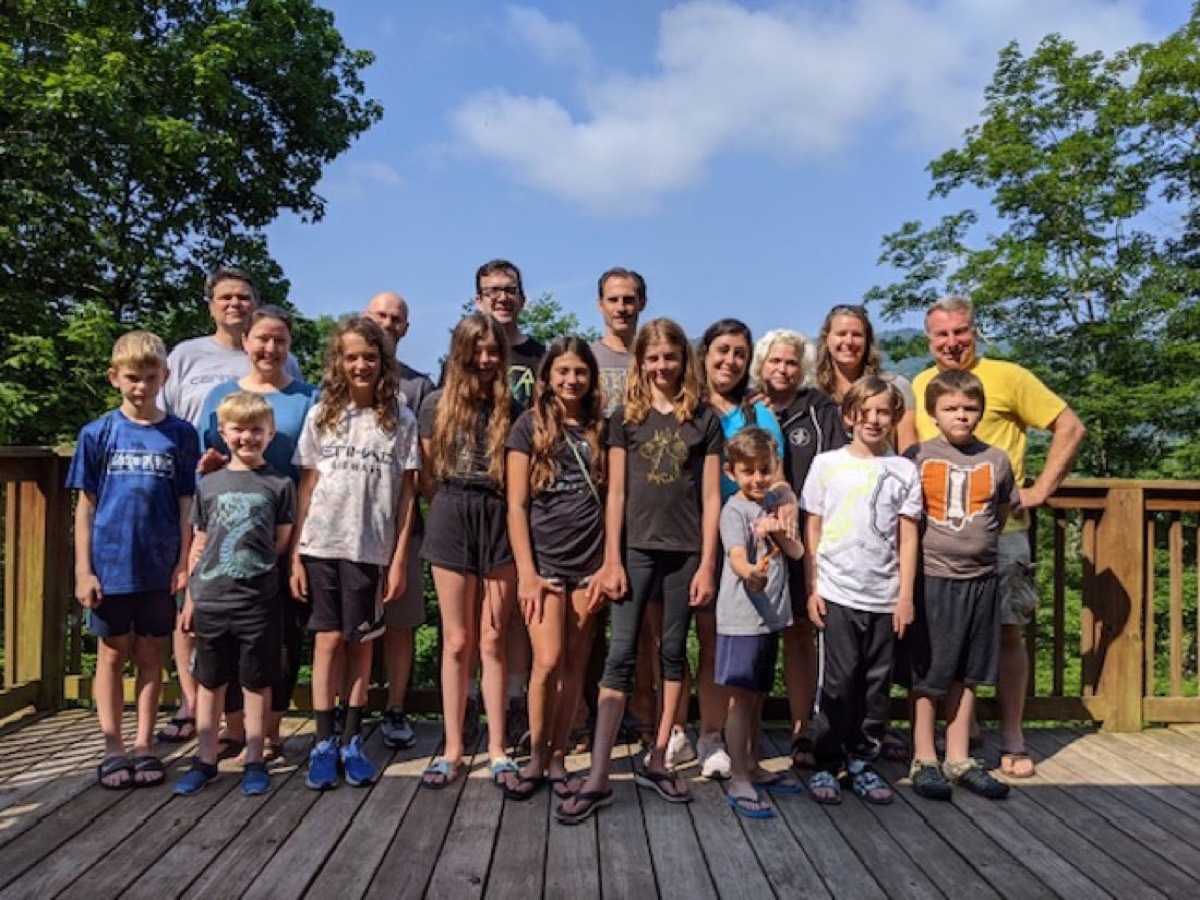The full Chuckwagon Gang, adults and kids, lined up on a sunny cabin deck with trees behind them
